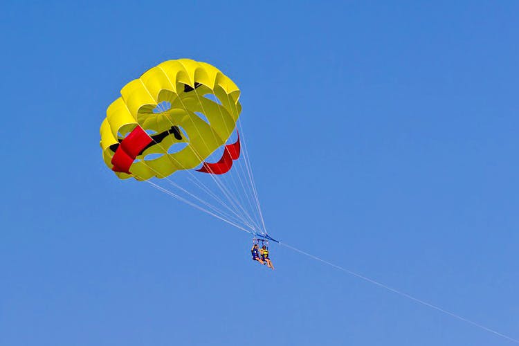 Parachute,Parachuting,Parasailing,Kite sports,Sky,Yellow,Extreme sport,Air sports,Air travel,Paragliding